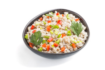 Pearl barley porridge with vegetables in blue ceramic bowl isolated on white background. Side view, close up.