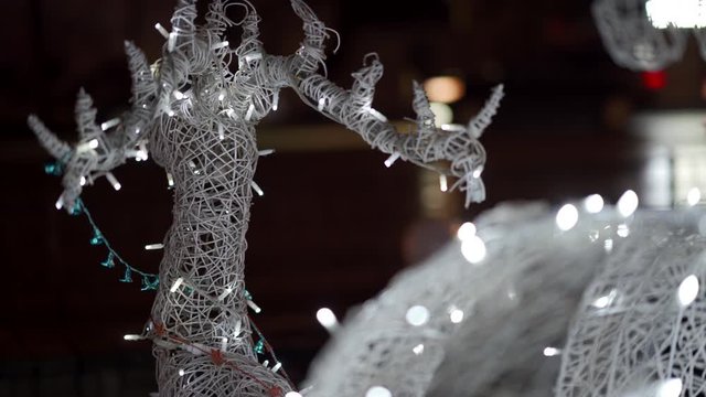 Christmas decorations on illuminated night city street, reindeer drawn carriage sculpture made from luminous Christmas lights.