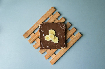 A delicious piece of toast with chocolate spread and banana slices on a modern kitchen countertop with a vintage wooden surface