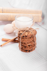 Oatmeal cookies, cinnamons and a glass of milk on a white table
