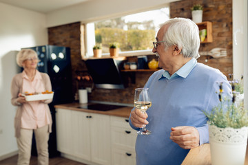 Happy senior man talking to his wife who is preparing food in the kitchen.