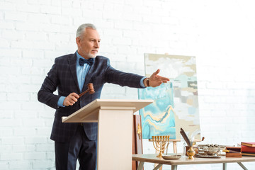 handsome auctioneer holding wooden gavel and pointing with hand during auction