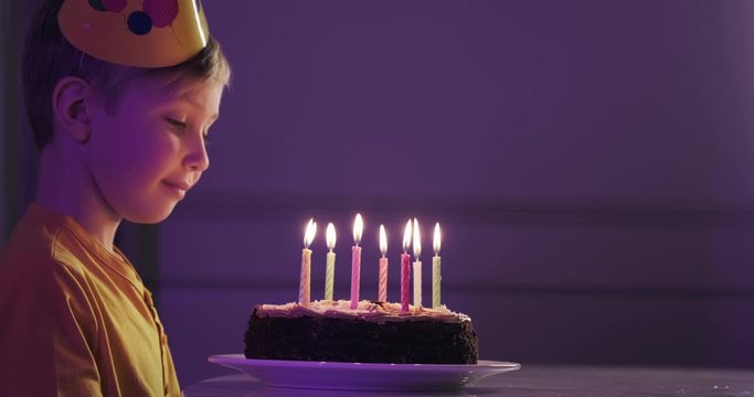 Cute boy blows out candles on a cake on his birthday.  Happy child looks at a cake with candles. Child looks at the cake and makes a birthday wish. Boy celebrates his birthday. Happiness concept