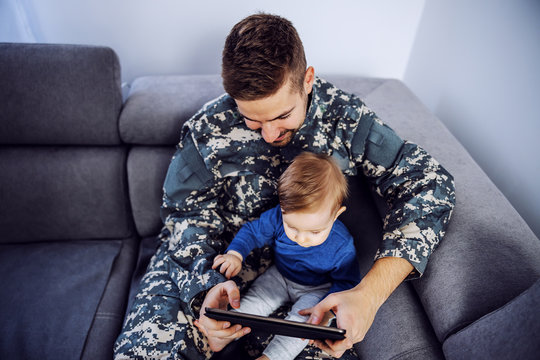 Top view of brave soldier making up for the lost time with his son. Man holding toddler in lap, tablet in hands and watching cartoons. - Powered by Adobe