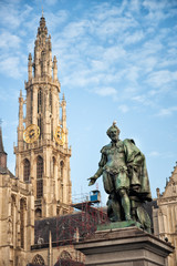 Obraz premium Vertical view of bell tower of Cathedral of Our Lady in Antwerp, UNESCO world heritage site in Belgium with statue of Pieter Paul Rubens with pigeon on his head in front. Travel tourism in Benelux.