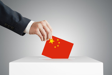 Man putting a voting ballot into a box with Chinese flag.