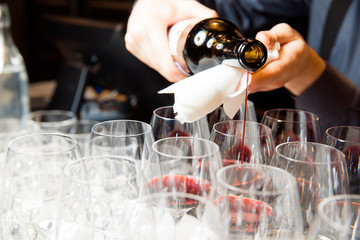 The waiter pours red wine into glasses.