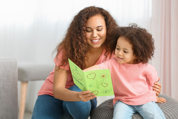 African-American woman with greeting card for Mother's Day received from her little daughter at home