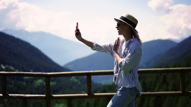 Excited caucasian female tourist using roaming network connection during trip to mountains making video call, happy young woman waving saying hello to travel blog followers on smartphone. Slow motion