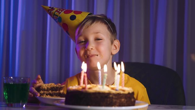 Cute boy eats cake on his birthday.  Happy child takes a piece of celebration cake and then bite it and swallow.  Happy white  boy celebrates his birthday. Caucasian cheerful child and birthday cake