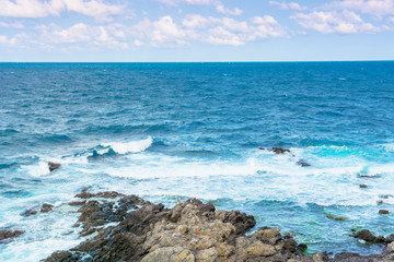 rocky sea shore in the afternoon. blue waves crashing the coast. fluffy clouds above the horizon.