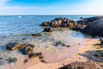 rocks on the sea beach in the morning. calm sunny weather. secluded place. fluffy clouds above the horizon.