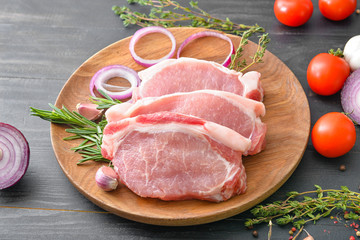 Plate with raw pork meat, spices and vegetables on dark wooden background