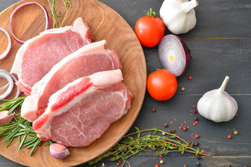 Plate with raw pork meat, spices and vegetables on dark wooden background