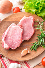 Plate with raw pork meat and vegetables on table