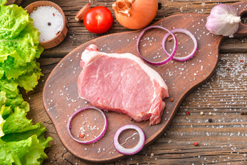 Board with raw pork meat, vegetables and spices on wooden background