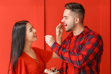 Beautiful young couple with tasty chocolate on color background