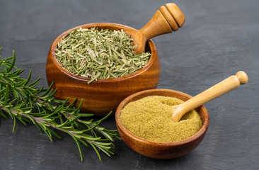 A wooden bowl with whole dried rosemary and a spice shovel,  a small wooden bowl with ground...