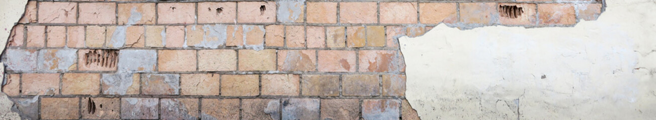 Obraz premium Old, multicolored brick with ruined plaster. Background texture for advertising or graffiti design with free space for text. The peeling wall of the house with Windows and metal bars.