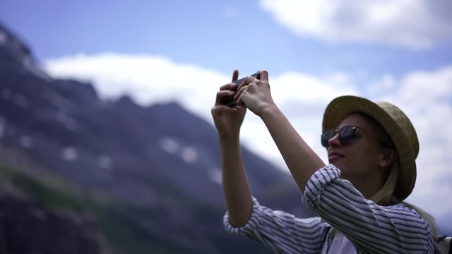 Smiling hipster girl traveler in hat using smartphone camera while making pictures for millennial travel blog, young woman wanderlust exploring nature landscape in mountains during summer vacations