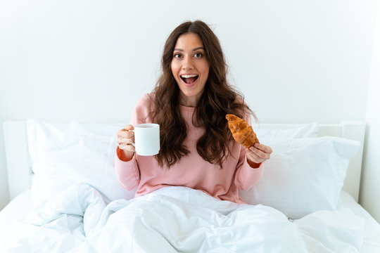 Happy optimistic young woman with croissant and coffee.