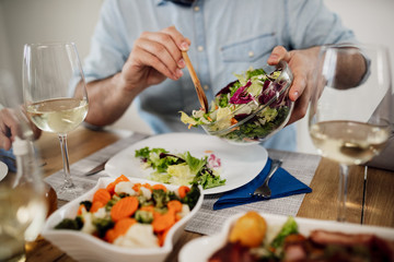 Close-up of man pouring salad while having lunch at dining table.