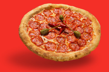 italian pizza with slices of salami and with red pepper, levitate, cast a shadow, on a red background, concept, in pastel colors