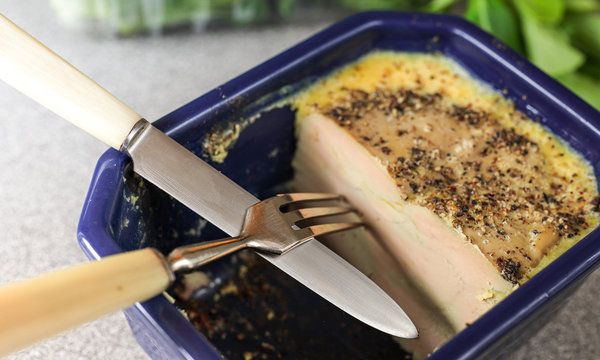 Homemade foie gras terrine, prepared according to a traditional French recipe with spices, with a knife and fork on a light background with fresh green salad