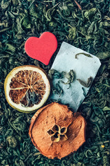 White tea bag on the background of loose tea, dried fruit: lemon, Apple, cinnamon, red heart. 
