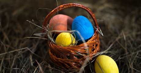 Easter eggs in a basket on a hay with a blurred background
