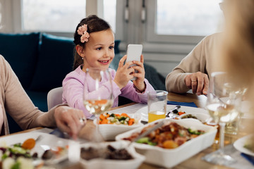 Cute little girl using mobile phone at dining table.