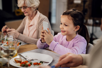 Cute girl playing games on mobile phone during lunch at dining table.