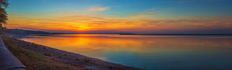 Panorama of colorful blue and golden sunset over the Kremenchug water reservoir in Svetlovodsk city, Kirovograd region, Ukraine. Beautiful romantic sunset view of the sea with sun reflection on water