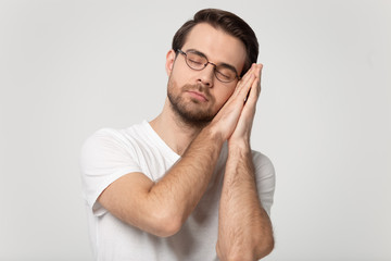 Tired young man in eyeglasses put head on folded hands.