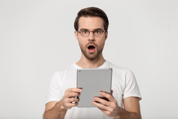 Surprised young man holding digital tablet, received unbelievable news.