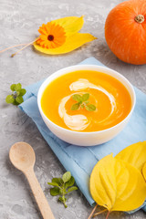 Traditional pumpkin cream soup with in white bowl on a gray concrete background with blue napkin. side view