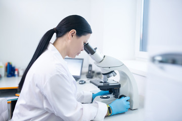 Dark-haired doctor in a white robe looking in microscope