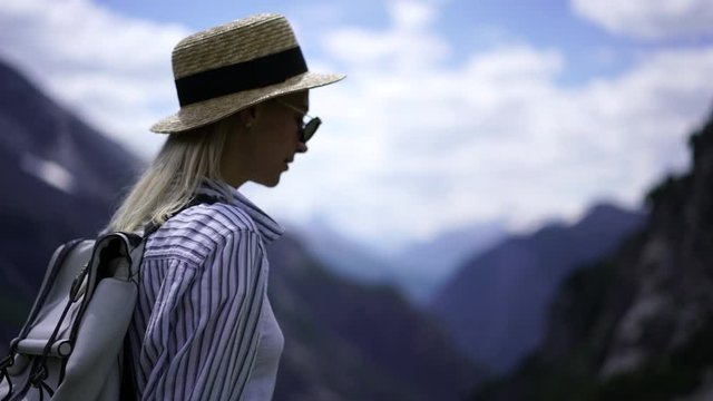 Back view of woman wanderlust with backpack walking on path in mountains landscape during trekking tour, female tourist in hat recreating actively in valley enjoying summer vacations
