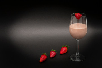 Vitamin cocktail in a wine glass, with one strawberry on top and three strawberries in a row below. Black background. Horizontal view. Close-up. Copy space