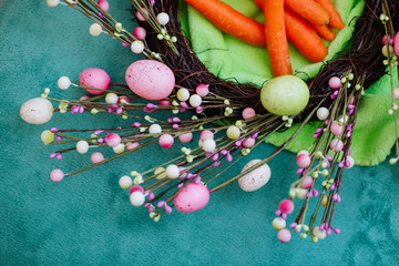 Colorful Easter decoration. Nest made of natural tree branches and decorated with pink painted eggs against blue green background. Top down view. 