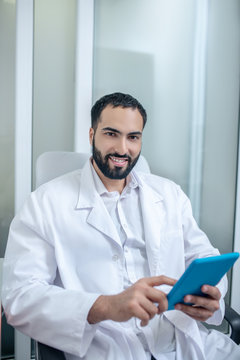 Male doctor in a white robe sitting in the chair and searfing internet