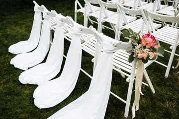Decorated luxury wedding ceremony place in the garden. White empty chairs decorated with flowers.