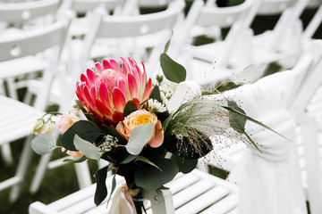 Decorated luxury wedding ceremony place in the garden. White empty chairs decorated with flowers.
