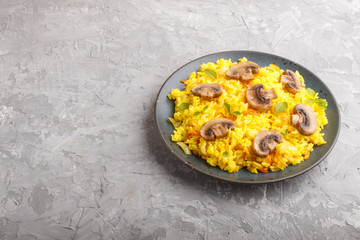 Yellow fried rice with champignons mushrooms, turmeric and oregano on blue ceramic plate on a gray concrete background. side view.