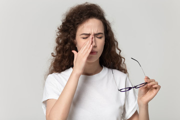 Tired young woman dropping eyewear, suffering from dry eyes syndrome.