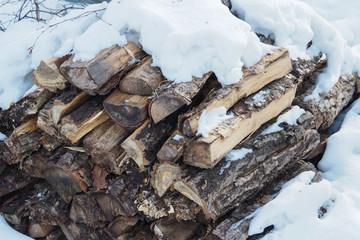 Folded chopped firewood with bark in the winter on a background of snow.