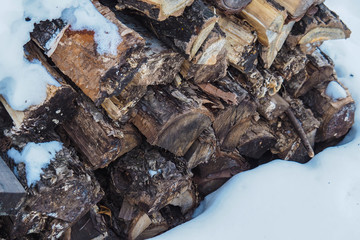 Folded chopped firewood with bark in the winter on a background of snow.