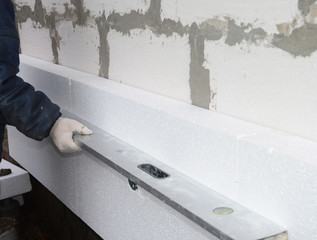  Builder holding spirit level in hand on the rigid styrofoam insulation wall. Rigid extruded...