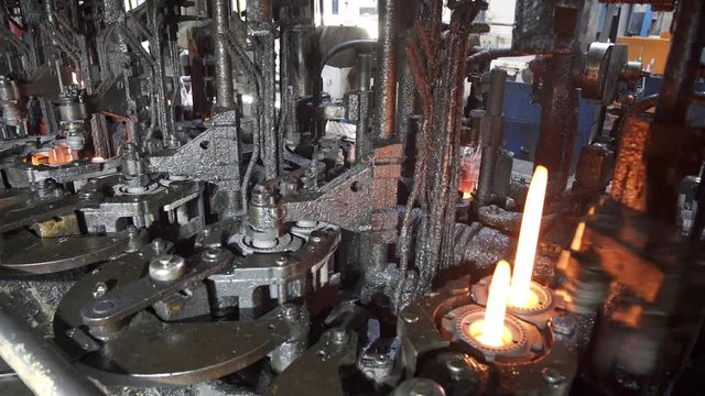 Automated process of forming a bottle of molten glass. The molten glass mass enters the mold and then into the glass blower where the bottle is formed. Production of glass bottles.