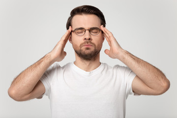 Stressed young guy in eyeglasses suffering from headache.